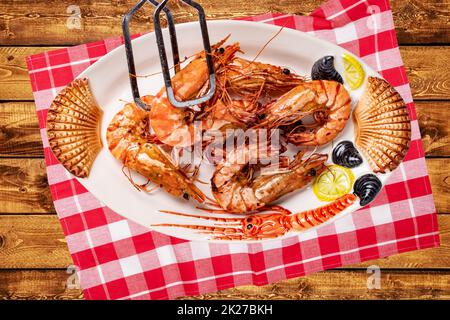 Genießen Sie frisch gegrillte große Garnelen oder Garnelen auf einem bunten Teller mit Meeresfrüchten auf einem rustikalen Tisch mit kariertem Stoff. Gesundes Lebensmittelkonzept. GRILLSPEZIALITÄTEN. Hintergrund für Meeresfrüchte. Weltraumwerbung. Stockfoto