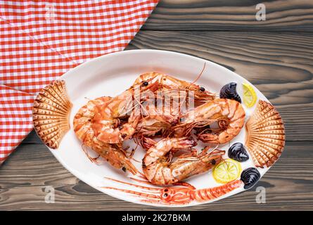 Genießen Sie frisch gegrillte große Garnelen oder Garnelen auf einem bunten Teller mit Meeresfrüchten auf einem rustikalen Tisch mit kariertem Stoff. Gesundes Lebensmittelkonzept. GRILLSPEZIALITÄTEN. Hintergrund für Meeresfrüchte. Weltraumwerbung. Stockfoto