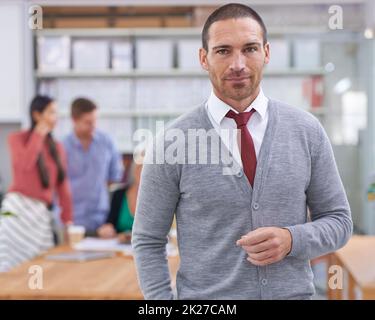 HES zuversichtlich, Erfolg zu haben. Ein hübscher junger Mann, der mit Kollegen im Hintergrund steht. Stockfoto