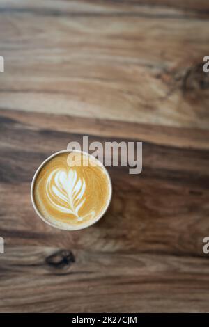 Cappuccino-Kaffee mit wunderschönem Muster auf Schaum in Eco Craft-Glas auf dem Tisch beliebtes Kaffeetassenkonzept. Blick von oben. Stockfoto