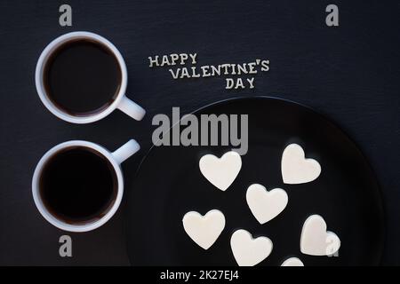 Zwei Tassen Kaffee und Schokoladenbonbons mit weißer Herzform - Aufschrift Happy Valentine Stockfoto