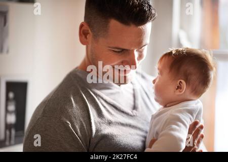 In den Augen meiner Tochter sehe ich, wer ich sein möchte. Ein junger Vater hält sein entzückendes Mädchen in der Hand. Stockfoto