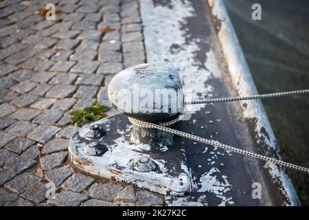 Ein gusseiserner Poller, um den ein Seil gewickelt ist und der ein Schiff festhält. Stockfoto