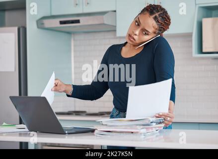 Schwarze Geschäftsfrau, die von zu Hause aus mit freiberuflicher, multitasking-Papierarbeit mit Laptop und Mobiltelefon-Audioanruf arbeitet. Internet-Technologie in der Küche Stockfoto