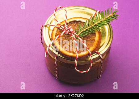 Hausgemachte Marmelade in einem dekorierten Glas mit Orangenscheibe und Tannenbaum. Wintergeschenk Stockfoto