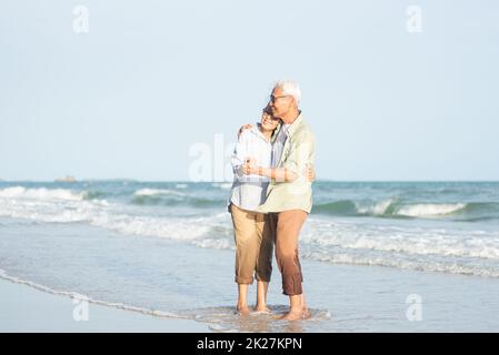 Glückliches asiatisches Seniorenpaar lächelt, tanzt und entspannt am Strand