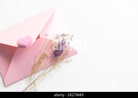 Flach auf einem weichen rosa Hintergrund Umschlag mit Herzen legen. Valentinstag- und Hochzeitskonzept. Liebeserklärung Stockfoto