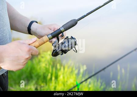 Eine Angelrute mit einer Drehrolle in den Händen eines Fischers. Hintergrund der Fischerei. Erholung im Freien. Stockfoto