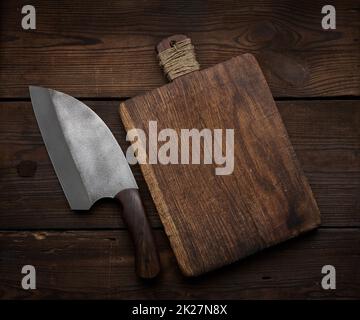 Küchenmesser aus Metall und leeres Holzschneidebrett auf einem Tisch aus braunen Holzbrettern, Draufsicht Stockfoto