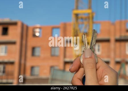 Bau eines neuen Gebäudes oder eines neuen Wolkenkratzers.Baustelle.Hände halten die Schlüssel für ein neues Haus.Hypothek für den Bau von Wohnungen.Immobilien und Grundstücke kaufen.Schuldverschreibungen Stockfoto