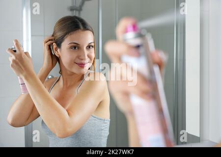 Junge Frau, die trockenes Shampoo auf ihr Haar aufwendet, bevor sie ausgeht. Schnelle und einfache Möglichkeit, graue Haare mit Instant-Spray-Farbstoff zu decken. Stockfoto