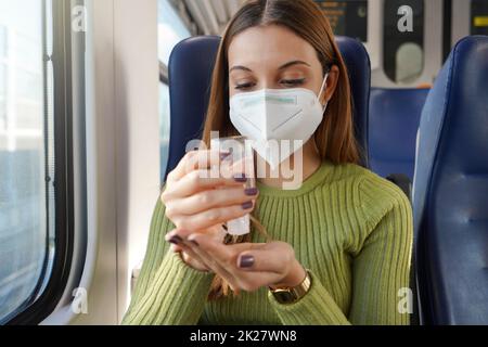 Geschäftsfrau im Zug mit obligatorischer Gesichtsmaske, die die Hände mit Alkoholgel desinfiziert. Antiseptisches, Hygiene- und Gesundheitskonzept. Stockfoto