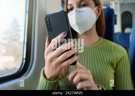 Trainieren Sie den Passagier mit der Smartphone-App während der Fahrt zur Arbeit und tragen Sie eine Gesichtsmaske. Konzentrieren Sie sich auf das Telefon. Stockfoto