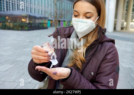 Frau mit KN95 FFP2 Maske, die Alkoholgel verwendet und ihre Hände auf der Straße der Stadt desinfiziert Stockfoto