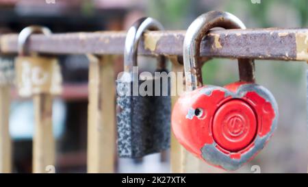 Schäbiges rotes Schloss in Herzform. Valentinstag-Liebeskonzept. Ein Vorhängeschloss, das an einem Metallgeländer hängt, ist ein Zeichen ewiger Liebe. Die Tradition, ein Schloss mit einem Zaun zu errichten Stockfoto