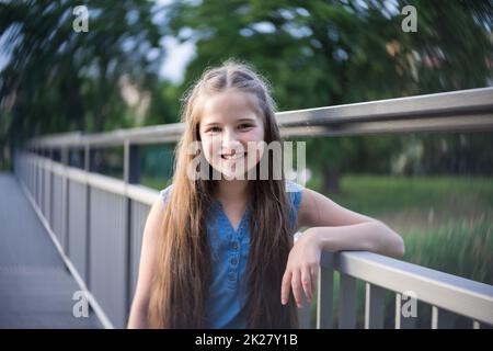 Portrait eines schönen Mädchens mit langen Haaren, das auf einer Brücke steht. Stockfoto