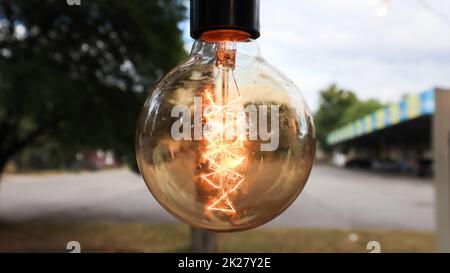 Edison Glühlampen hängen im Retro-Loft-Stil. Kantinendekoration Nahaufnahme. Straßendekor Helle Laternen in warmem Licht. Weicher Fokus, unscharfer Straßenhintergrund Stockfoto