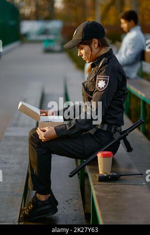 Polizeibeamter, der in der Nähe des Parks Donut isst Stockfoto