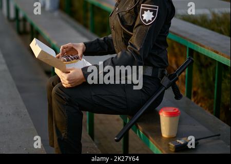 Polizeibeamter, der in der Nähe des Parks Donut isst Stockfoto