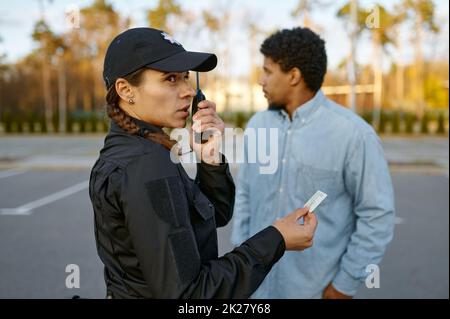 Weiblicher Polizist, der das Ausweisdokument der männlichen Passanten überprüft Stockfoto