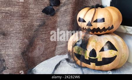 Kürbis mit einem gruseligen Gesicht auf einem Holztisch. Das Innere des Hauses ist mit Kürbissen und Spinnennetzen für den Feiertag von Halloween dekoriert. Stockfoto