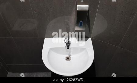 Weißes Keramik-Waschbecken mit Chromhahn in der Toilette mit grauen Fliesen Stockfoto