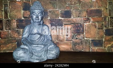 Ukraine, Kiew - 10. Juni 2020. Statuette des Segens Buddhas auf einem hölzernen Regal vor einer Steinmauer. Keramikfiguren und -Figuren Dekoration oder Symbol im Innenraum. Stockfoto