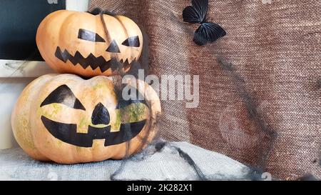 Kürbis mit einem gruseligen Gesicht auf einem Holztisch. Das Innere des Hauses ist mit Kürbissen und Spinnennetzen für den Feiertag von Halloween dekoriert. Stockfoto