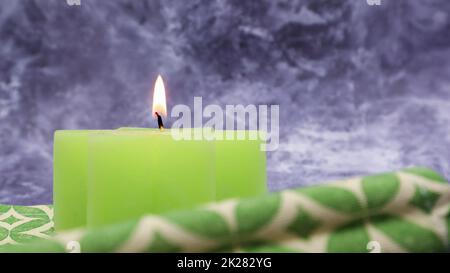 Komposition mit einer grün beleuchteten Kerze auf einem Tisch mit einer grünen Leinenserviette vor einem wunderschönen grauen Marmorhintergrund. Platz für Ihre SMS. Weihnachtsdekorationen. Stockfoto