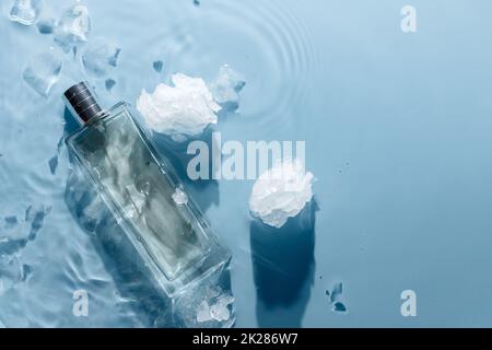 Parfüm-Flasche auf blauem Wasser gewellter Hintergrund mit Eisstücken. Frisches kühles Wasserduft-Konzept Stockfoto