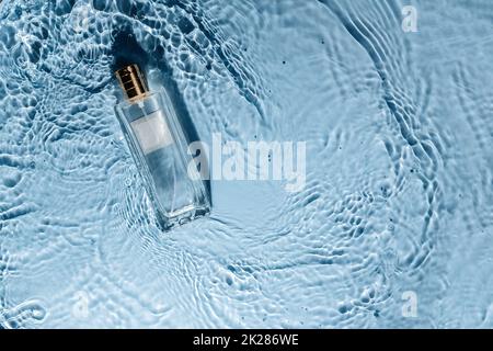 Parfüm-Flasche auf blauem Wasser welligen Hintergrund. Frisches Meeresduft-Konzept. Frauen- und Männeressenz. Stockfoto