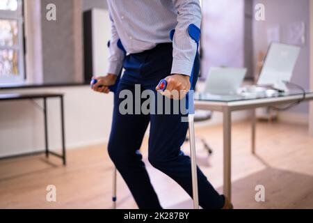 Arbeiter Mit Krücken Am Arbeitsplatz Oder Im Büro Stockfoto