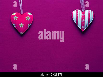Zwei weiße rosa Metallherzen auf dunkelrosa Papierhintergrund Stockfoto