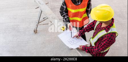 Der Architekt und der Kunde, der mit ihm spricht, helfen bei der Erstellung eines Plans mit dem Bauplan des Gebäudes auf dem Boden der Baustelle. Asiatischer Ingenieur Vorarbeiter, Mann und Frau, Meeting und Planung von Bauarbeiten, Draufsicht Stockfoto