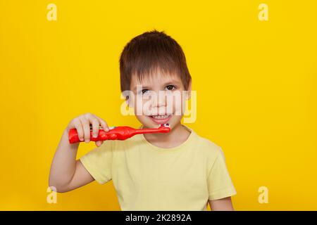 Ein glücklicher kleiner Junge putzt sich die Zähne mit einer Zahnbürste auf gelbem Hintergrund. Gesundheitspflege, Mundhygiene. Stockfoto