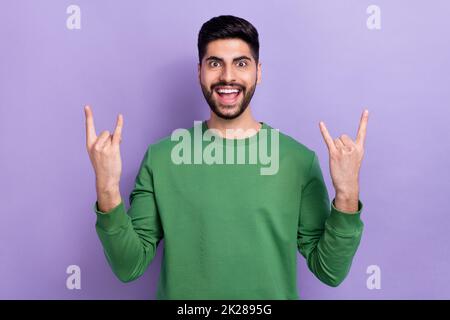 Foto von schönen stilvollen beeindruckt unachtsamen Kerl tragen grünen Pullover zeigt Hörner Schwermetall auf violettem Hintergrund isoliert Stockfoto