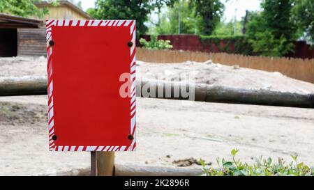 Rotes, leeres metallisches Schild an einem Zaun für das Design von Vorlagen. Leeres Formular. Kopieren Sie Platz für Ihren Text oder Ihr Logo. Stockfoto