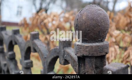 Fragment einer gusseisernen Zaunnaht. Ein alter gusseiserner schmiedeeiserner Zaun mit künstlerischer Schmiedung vor dem Hintergrund eines Herbstparks. Selektiver Fokus. Stockfoto