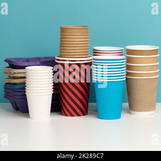 Stapel von Papier Einweg mehrfarbigen Tassen und stehen auf weißem Tisch, blauer Hintergrund Stockfoto