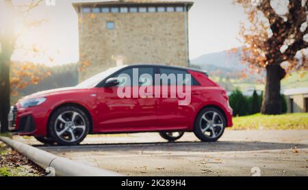 Ein unscharfer roter Geländewagen parkt auf dem Parkplatz der Stadt. Seitenansicht des Elektrofahrzeugs auf dem Parkplatz. Elektrofahrzeugkonzept. Road Trip in Europa. Automobilindustrie. Umweltfreundliches Auto. Stockfoto