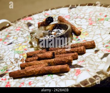 Zigarettenanzünder und Aschenbecher auf dem Tisch der verleimten Stücke der Töpferei. Hausgemachte Zigarren aus grünen Tabak auf einem keramischen Tisch verlässt. Aschenbecher und Zigarren. Stockfoto