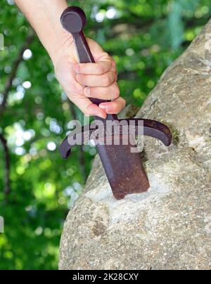 Hand des Ritters, der versucht, das Excalibur-Schwert zu extrahieren, das in den Felsen im verzauberten Wald eingebettet ist Stockfoto