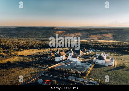 Luftaufnahme der orthodoxen Kirche bei Sonnenuntergang – wunderschöne rumänische Landschaft mit smaragdgrünen Feldern und Wiesen. Stockfoto