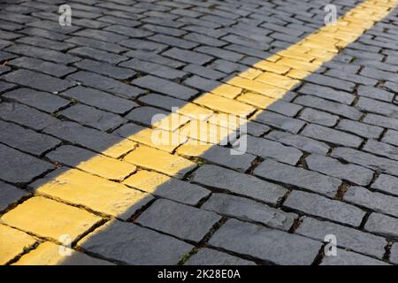 Steinpflaster, gepflasterte Straße. Straßenmarkierung, gelbe Linie auf Fliesen Stockfoto