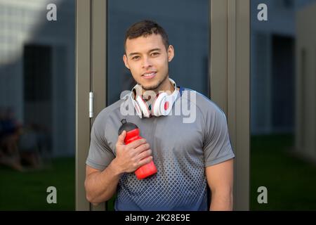 Lächelnder junger lateiner, Wasserflaschenläufer, Outdoor-Sport-Fitnesstraining Stockfoto