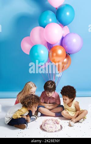 Wunsch nach einem Ballon. Eine Gruppe von Kindern blasen die Kerzen auf einem Geburtstagskuchen. Stockfoto