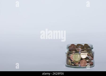 Geld in einem Flachglas mit vielen verschiedenen Euro-Münzen eingespart, um finanzielle Unabhängigkeit mit Grau zu gewährleisten Stockfoto