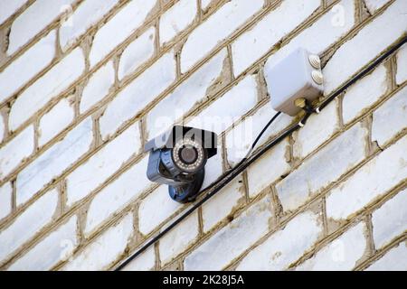 Video Kamera mit Beleuchtung ist an der Wand hängen. Wand aus weißen Stein und einer Videokamera mit Kabel. Stockfoto