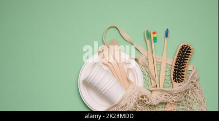 Weißer Baumwollbeutel, Pappbecher und Holzzahnbürsten auf grünem Hintergrund, Kopierbereich Stockfoto