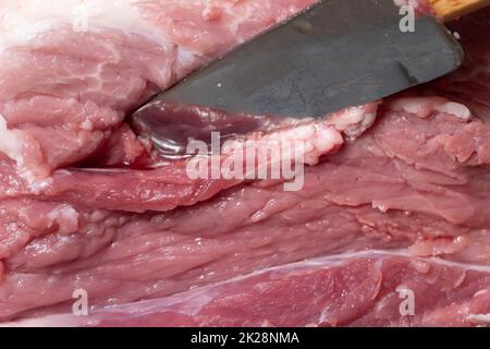 Schneiden Sie das Schweinefleisch oder Rindfleisch mit einem Messer auf dem Tisch in Nahaufnahme. Zubereitung von Fleischgerichten und Nahrungsmitteln. Stücke von rotem Fleisch für Shish Kebab, Barbecue oder Kebab. Rohes frisches Fleisch wird mit einem Messer geschnitten. Rezept Stockfoto